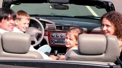 stock-footage-parents-and-two-kids-sit-in-cabriolet-and-look-backward-then-turn-view-from-behind-at-sunny-day.jpg