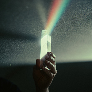 Hand holding a prism, casting a rainbow of light.