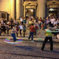 People dancing and hula hooping on steps of a historic building.
