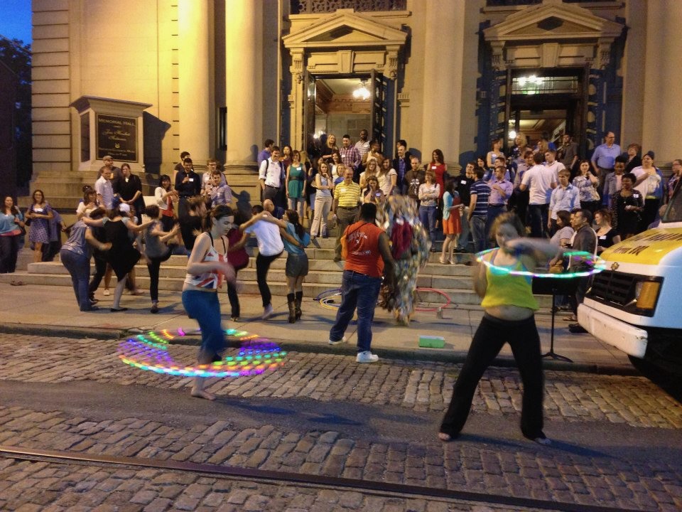 People dancing and hula hooping on steps of a historic building.
