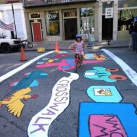A young girl riding her bike over a newly painted art crosswalk